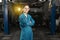 A young woman in work clothes, an apprentice stands next to the car and is proud and happy in the garage with protective