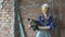 The young woman in working clothes and a construction helmet with the puncher against the background of red brick camps