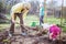 Young woman working in garden while her little daughter playing with spade beside her