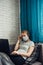 Young woman working at home during quarantine. Sick woman wearing face mask with laptop, lying on sofa. Remote office, self-