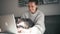 A young woman working on a laptop at home and holds a grey cat in her arms