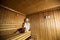 Young woman wrapped in a white towel relaxing in wooden sauna