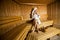 Young woman wrapped in a white towel relaxing in wooden sauna
