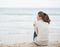 Young woman wrapping in sweater while sitting on lonely beach