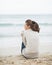 Young woman wrapping in sweater while sitting on lonely beach