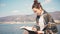 A young woman writer sits on a pier and writes notes in a notebook