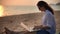 A young woman writer sitting on the beach with her laptop and typing a text.