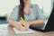 Young woman writing notes at laptop closeup