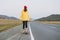 Young woman in yellow hoodie and red hat on skateboard on the road against beautiful mountain landscape, Chuysky tract, Altai