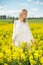 Young woman in yellow oilseed rape field posing in white dress