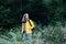 Young woman in yellow raincoat with backpack in forest. Caucasian female tourist resting forest walks. Young woman