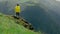 A young woman in a yellow raincoat climbs the slope and enjoys the magnificent scenery of the mountainous areas. Tourism