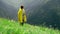 A young woman in a yellow raincoat climbs the slope and enjoys the magnificent scenery of the mountainous areas. Tourism