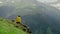 A young woman in a yellow raincoat is sitting on a cliff and enjoying the magnificent scenery of the mountainous regions