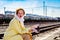 A young woman in a yellow raincoat with sunglasses in her hands sits on the platform of a railway station