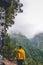 Young woman in yellow sweatshirt on viewpoint in Levada Caldeirao Verde, Madeira, Portugal. Green scenic mountains in mist, foggy