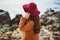 Young womanin brown cashmere coat standing on sand and holding maroon felt hat