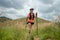 Young women active trail running across a meadow on a grassy trail high in the mountains in the afternoon with trekking pole