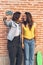 Young women couple making a selfie. Behind brick wall. Positive emotion and tolerance concept