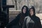 Young Women with dark long hair in black robes in front of an Old Wooden Water Mill. Witches. Halloween concept. Witchcraft