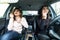 Young women distracted and laughing in car with cellphone and cosmetics