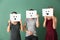 Young women hiding faces behind sheets of paper with drawn emoticons on color background