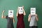 Young women hiding faces behind sheets of paper with drawn emoticons on color background