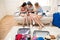 Young women packing suitcases for vacation and using smartphones at home,