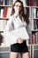 Young women stands near bookshelf