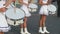 Young women weared in white short dresses play drums on parade on summer day.
