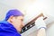 A young worker in a blue baseball cap and gloves inspects and maintains the air conditioner in the room.