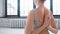 Young yoga trainer wearing beige top shows reverse namaste sitting on floor against window in light studio