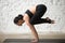 Young yogi attractive woman in Bakasana pose, white loft backgro