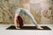 Young yogini practicing Chakrasana variation pose in pastel blue leggins and top