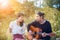 Younger asian man and woman relaxing playing guitar in park