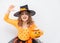 Younger blonde girl in orange witch costume with candy bucket pumpkin Halloween on white background.