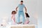 Youre the fun parent, just dont tell Mom. a man jumping on a bed with his two daughters.