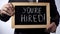 Youre hired with exclamation written on blackboard, businessman holding sign