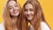 Youth and happiness. Close up portrait of two cheerful redhead twin sisters laughing to camera, orange background
