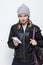 Youth Lifestyles. Portrait of Gloomy Caucasian Blond Girl in Warm Hat and Leather Jacket Posing With Cellphone and Backpack on