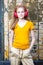 Youth and Teens Lifestyle. Positive Teenage Girl In Red Wireless Headphones Posing in Casual outfit Against Grunge Wall In Summer