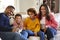 Youthful grandparents sitting with their grandchildren on sofa in the living room eating popcorn and laughing, front view, close u