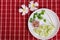 Yum tuna salad is small on a white plate, garnished with melons and fresh green coriander. Red and white plaid fabric background.