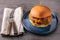 Yummy chicken burger with cheese on a blue round plate and cutlery on side