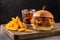 Yummy chicken burger with cheese, fries and a glass of cola on a wooden board on a dark background