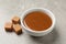 Yummy salted caramel in bowl and candies on grey table