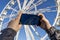 Zamora, Spain. March 20, 2021. A hand of a person with a mobile takes a picture of a white Ferris wheel with the blue sky in the b