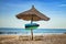 Zanzibar flag on wooden arrow sign. There are two sun loungers and a sun umbrella on the beach. It is a tropical