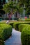 A zigzag garden pathway with shrubs and temple tree with water fountains in the background