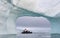 A zodiac full of tourist viewed through an arch in a large iceberg, Antarctica